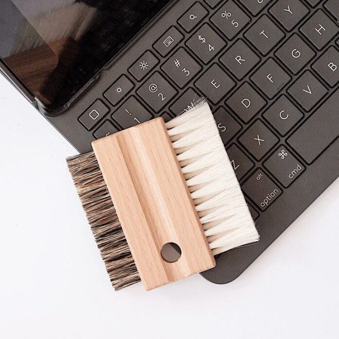Ręce trzymające laptopa odwróconego klawiaturą w dół z opadającym kurzem i brudem