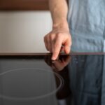 Woman holding finger on power button at electric stove