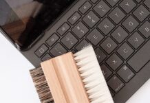 Brudna klawiatura laptopa – jak ją wyczyścić bez uszkodzenia delikatnych elementów? Ręce trzymające laptopa odwróconego klawiaturą w dół z opadającym kurzem i brudem