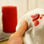 Bliski plan usuwania kropli czerwonego wosku z białego lnianego obrusu gorącym żelazkiem