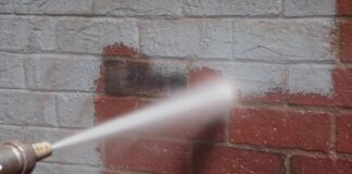 Piaskowanie elewacji ceglanej – kiedy można odsłonić surowy charakter cegły i jak to zrobić bezpiecznie? Robotnik w kombinezonie piaskuje ceglaną elewację starego budynku strumieniem piasku pod ciśnieniem